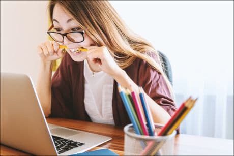 woman biting on a pencil in front of computer screen