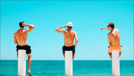 3 men sitting on a wall by the beach.